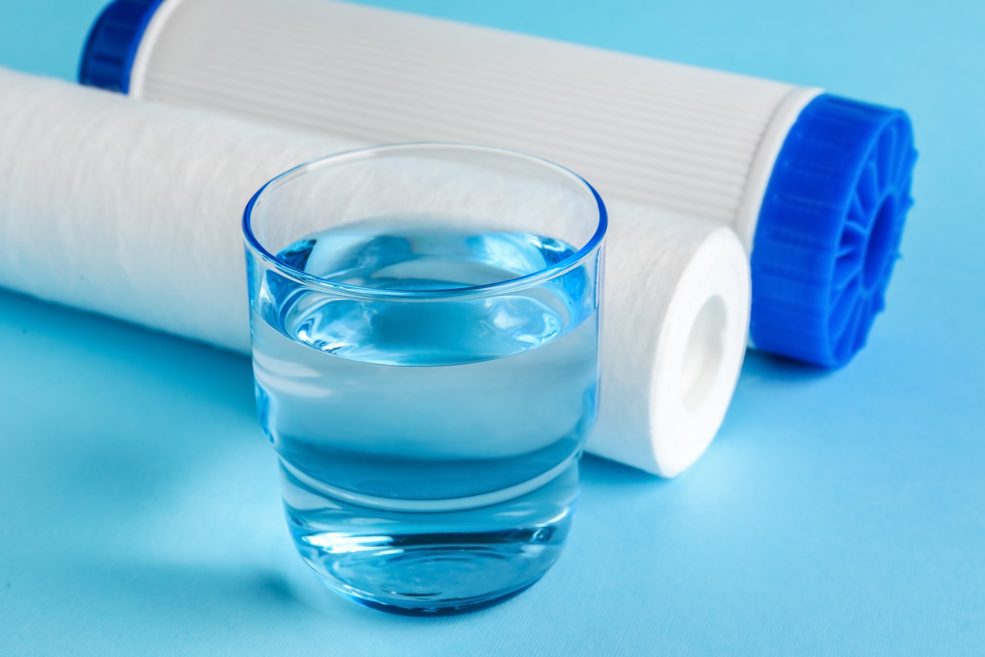 Glass of Liquid and Water Filter Cartridges on Blue Background